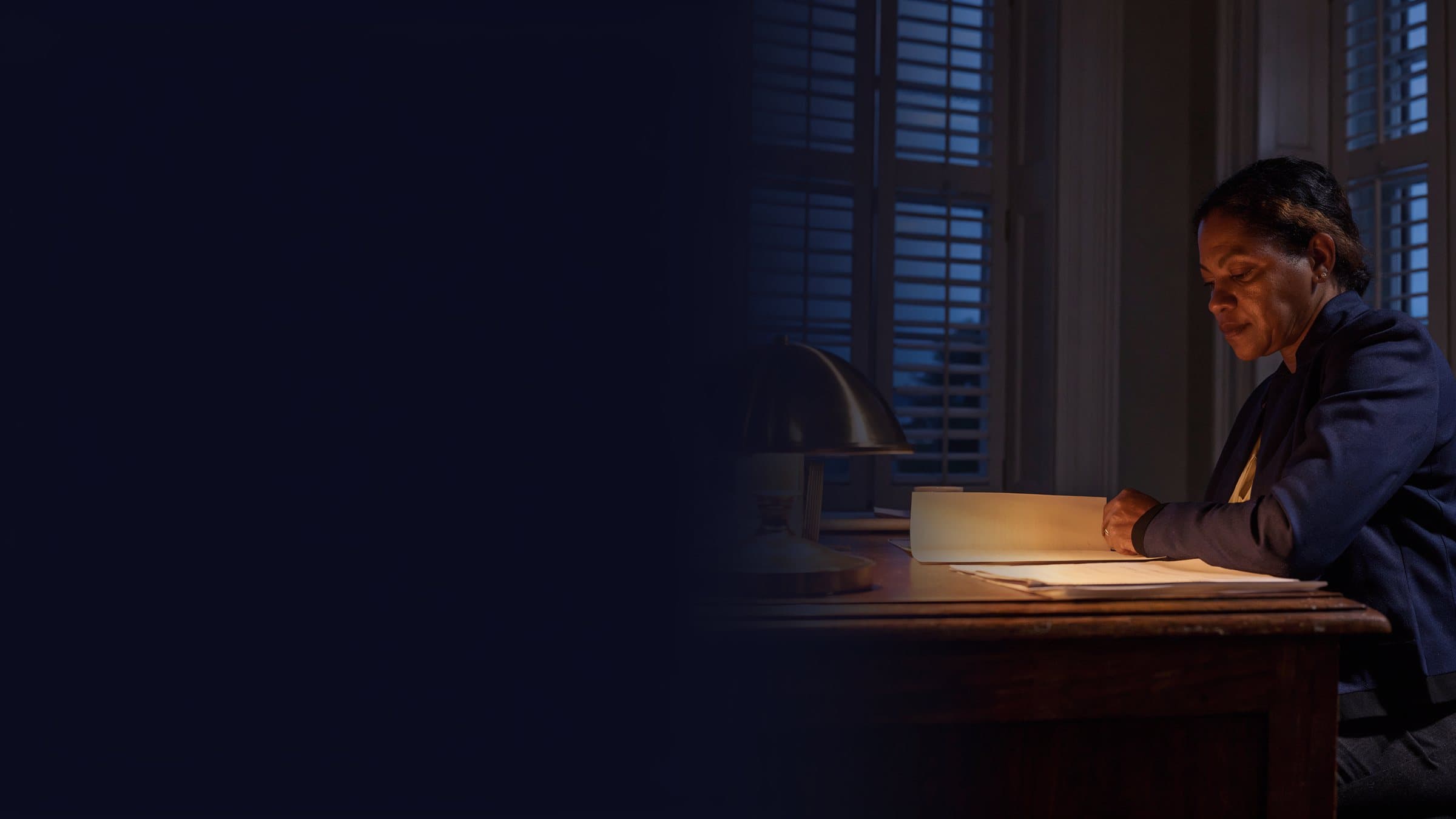 A compliance officer at a desk by a window, reading a document.