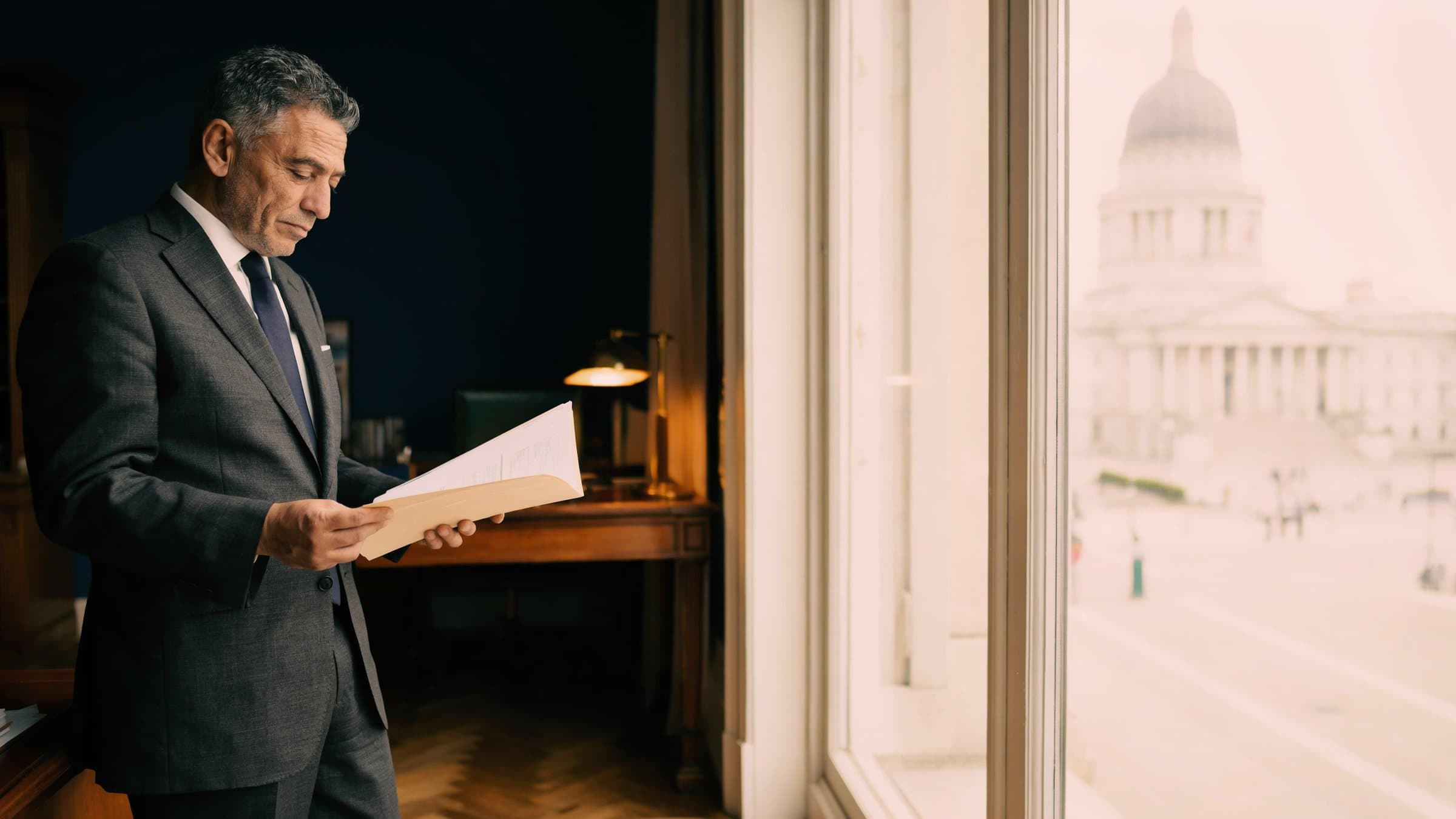 A trust officer reading a client file beside a window that looks onto a domed legislature.