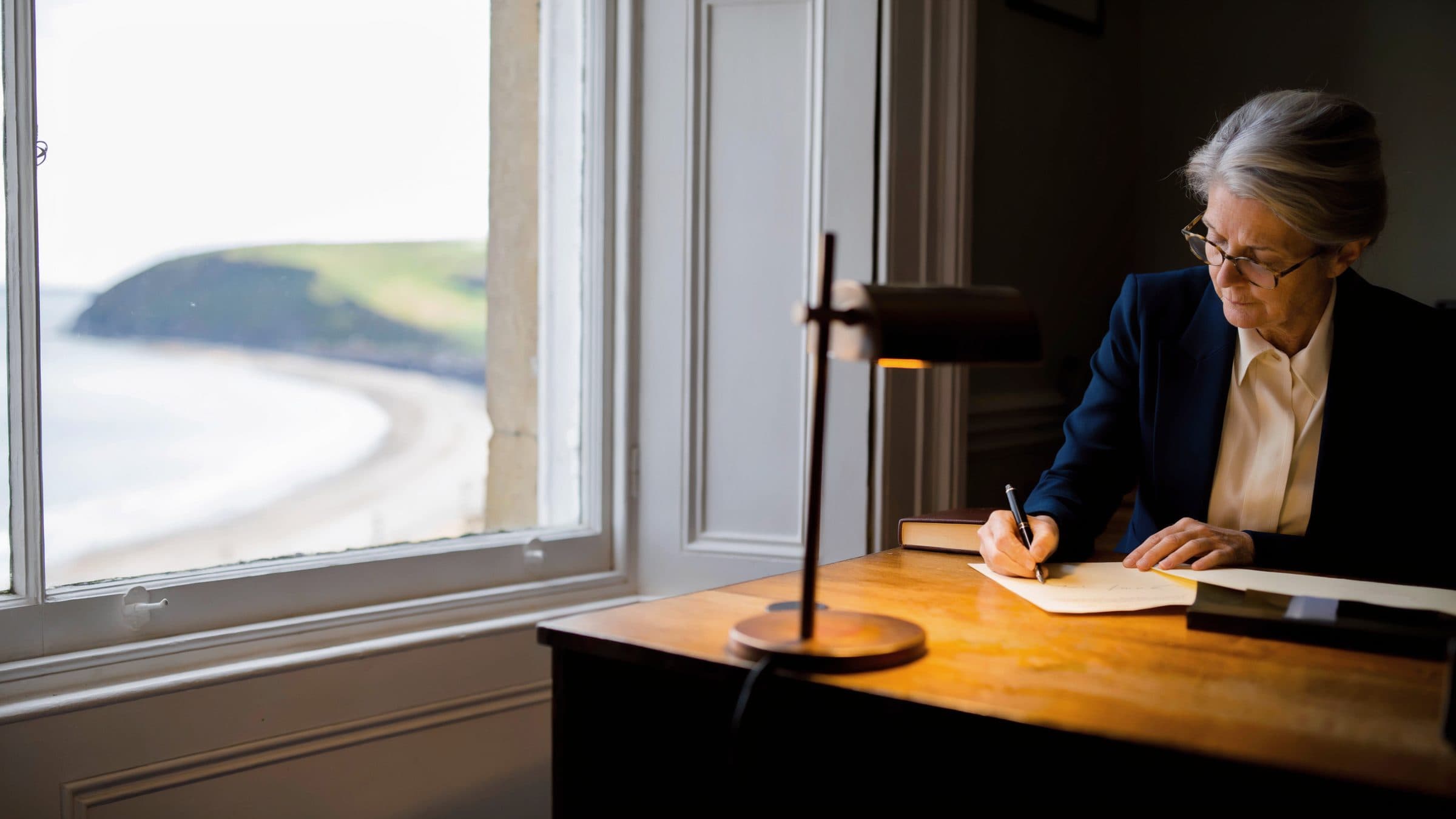 A trust officer signing a page at a desk beside a window that looks onto a wide bay.