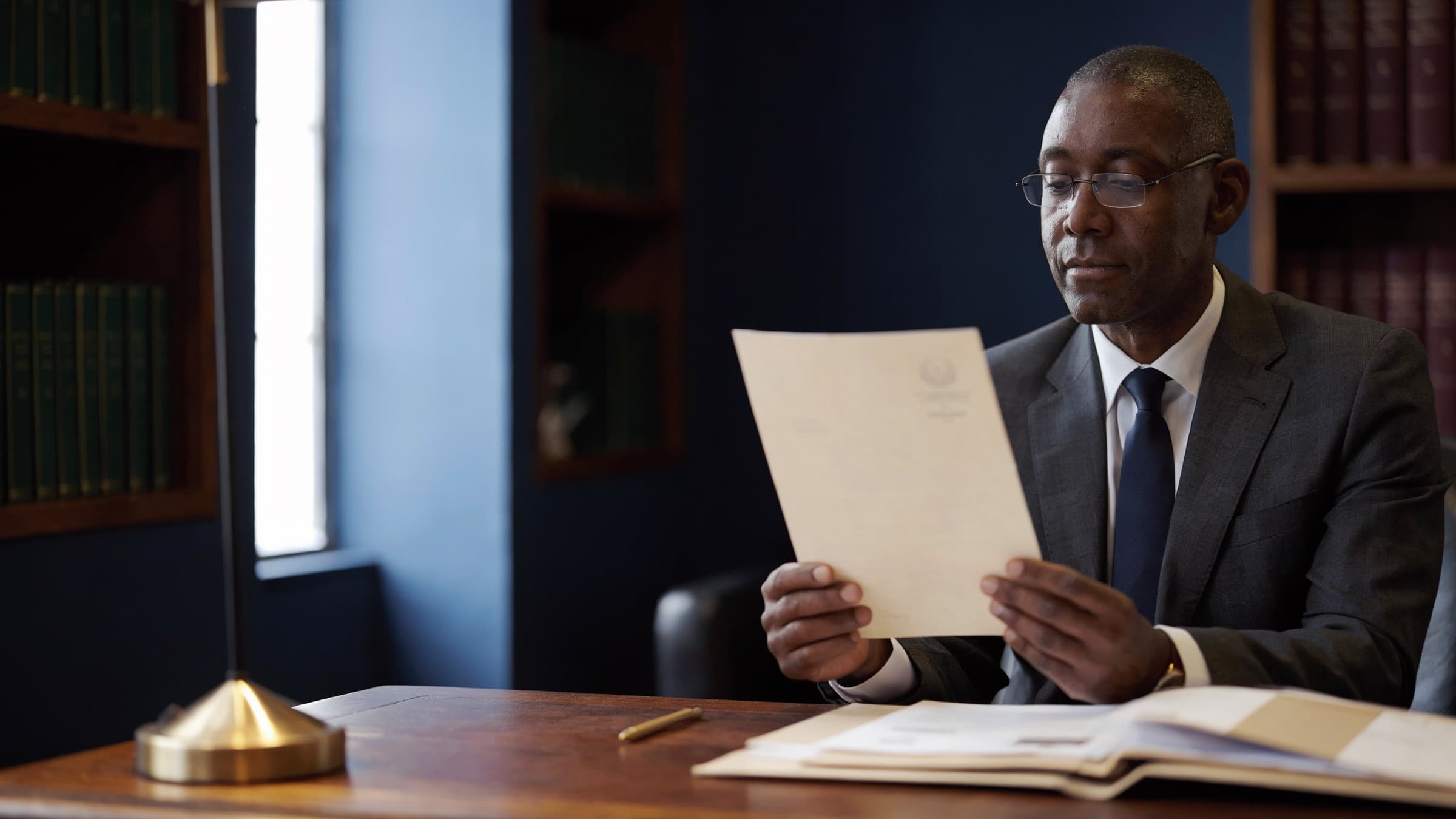 A compliance officer at his desk reading an official notice beside an open client file.