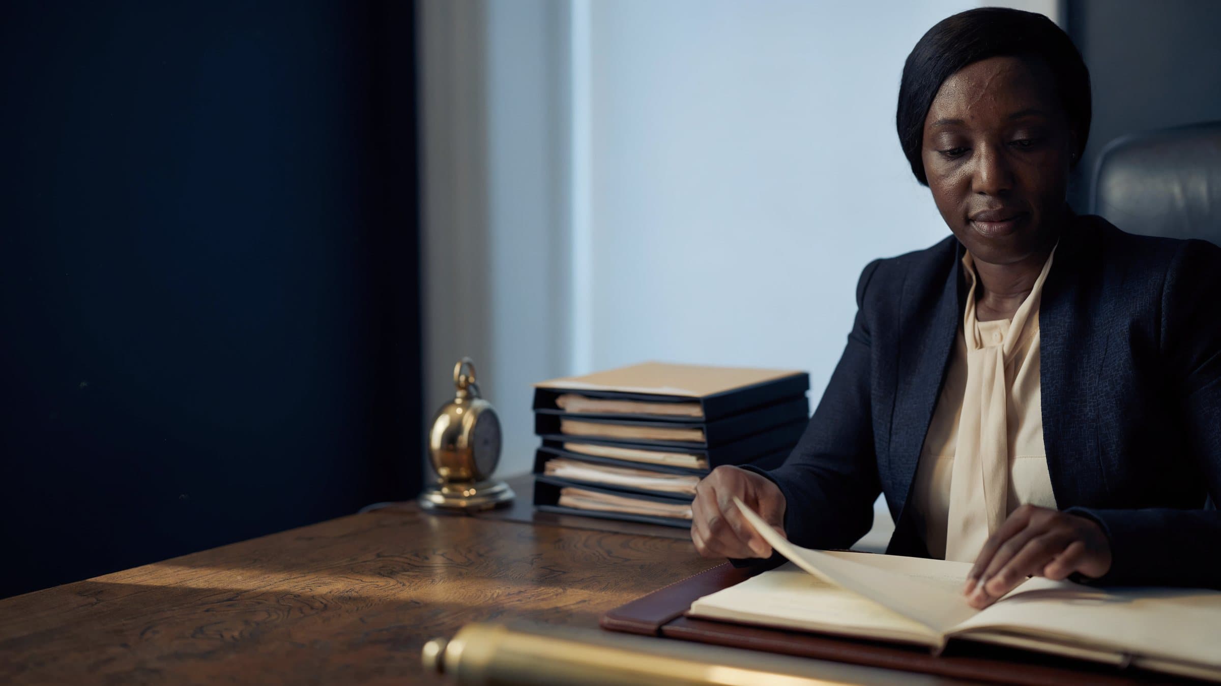 A trust officer at her desk in the early morning, turning a page of a desk diary.
